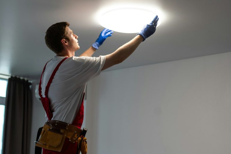 Electrician in uniform installing ceiling lamp indoors. Space for text